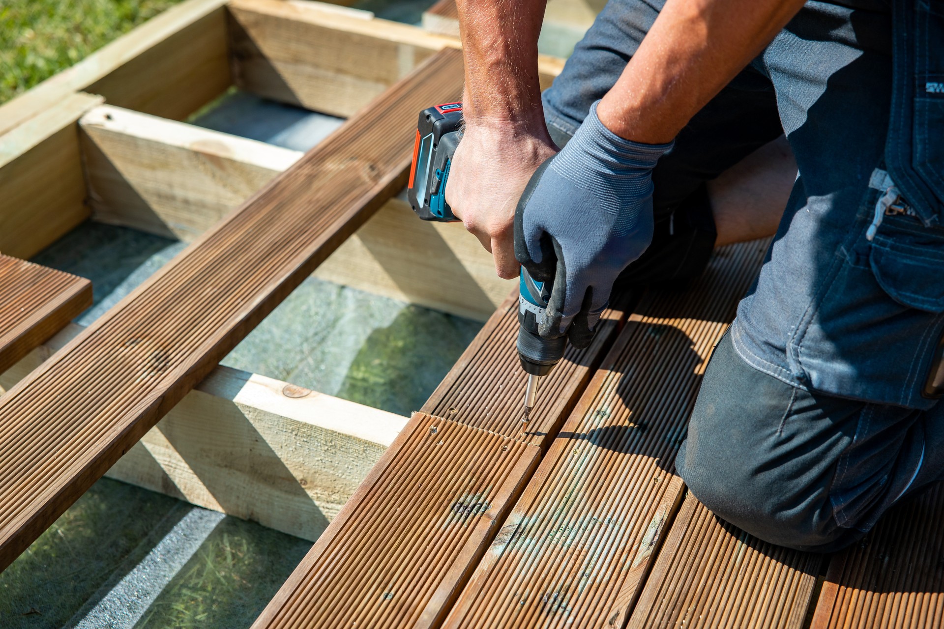 Deck construction, builder hand with electric screwdriver installing impregnated wooden boards